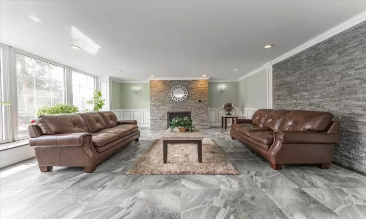 Living area featuring ornamental molding, wainscoting, a decorative wall, and a stone fireplace