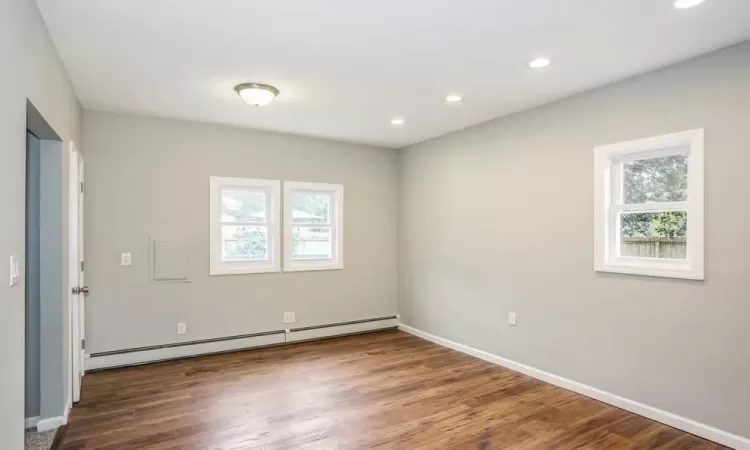 Empty room featuring recessed lighting, a baseboard radiator, a wealth of natural light, and wood finished floors