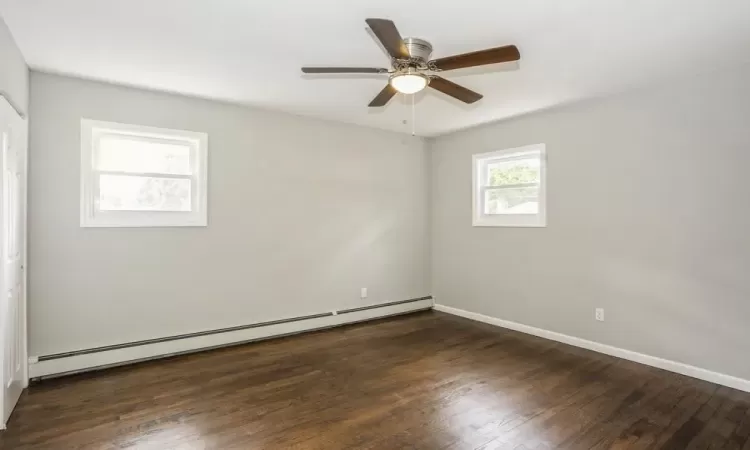 Unfurnished room with dark wood-type flooring, baseboards, baseboard heating, and a ceiling fan