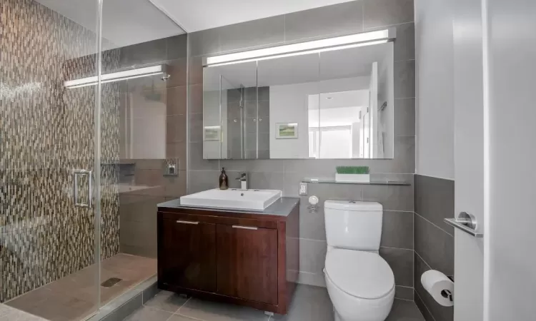 Bathroom featuring toilet, a stall shower, vanity, and tile walls