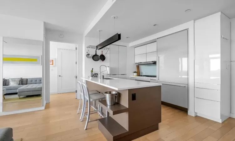 Kitchen featuring a breakfast bar, light wood-style flooring, white cabinets, a sink, and modern cabinets