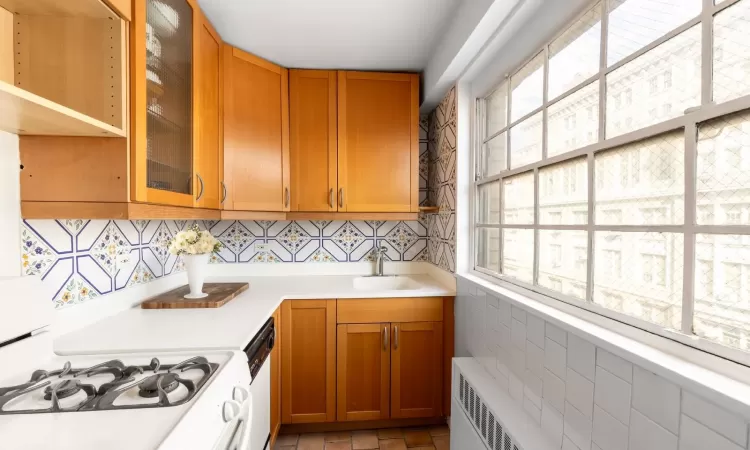 Kitchen featuring white appliances, a sink, light countertops, brown cabinets, and radiator heating unit