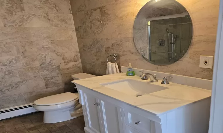 Bathroom featuring toilet, baseboard heating, tile walls, and vanity