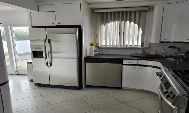 Kitchen featuring light tile patterned floors, white cabinets, appliances with stainless steel finishes, backsplash, and a sink