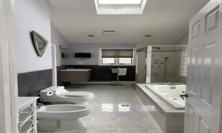 Full bathroom with a bidet, a relaxing tiled tub, visible vents, a tile shower, and lofted ceiling with skylight