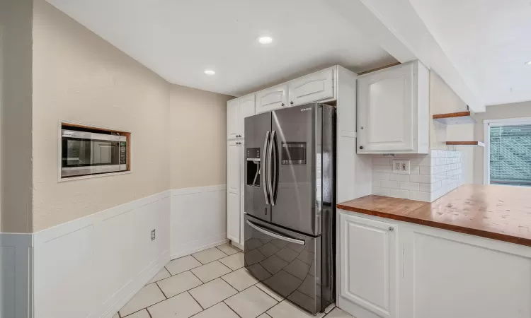 Kitchen featuring a wainscoted wall, stainless steel refrigerator with ice dispenser, light tile patterned floors, white cabinetry, and butcher block countertops