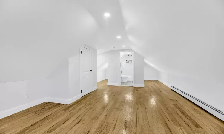 Additional living space with a baseboard heating unit, wood-type flooring, lofted ceiling, and baseboards