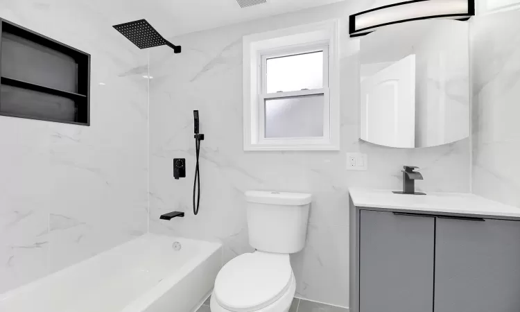 Bathroom featuring visible vents, toilet, bathtub / shower combination, vanity, and tile walls