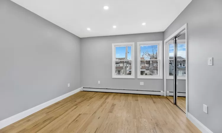 Empty room with light wood-type flooring, baseboards, baseboard heating, and recessed lighting