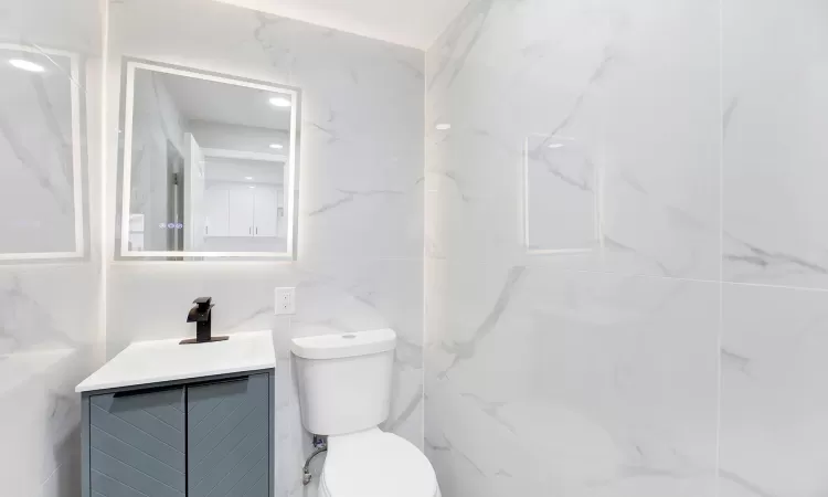 Bathroom featuring vanity, toilet, and tile walls