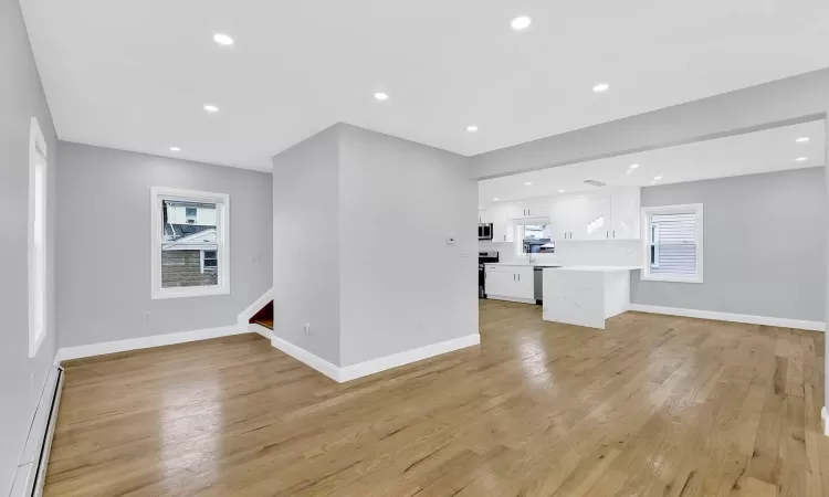 Unfurnished living room with light wood-style flooring, a baseboard heating unit, baseboards, and recessed lighting