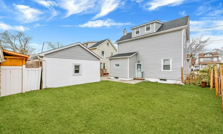 Rear view of house featuring a shingled roof, a patio area, a lawn, and fence