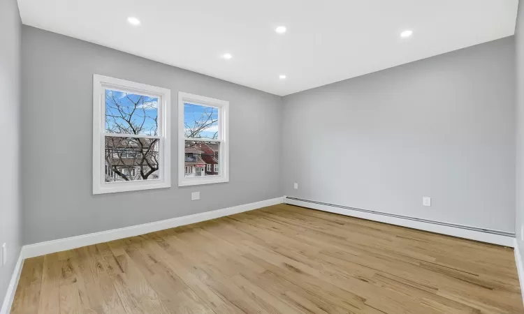 Empty room with a baseboard heating unit, recessed lighting, wood finished floors, and baseboards