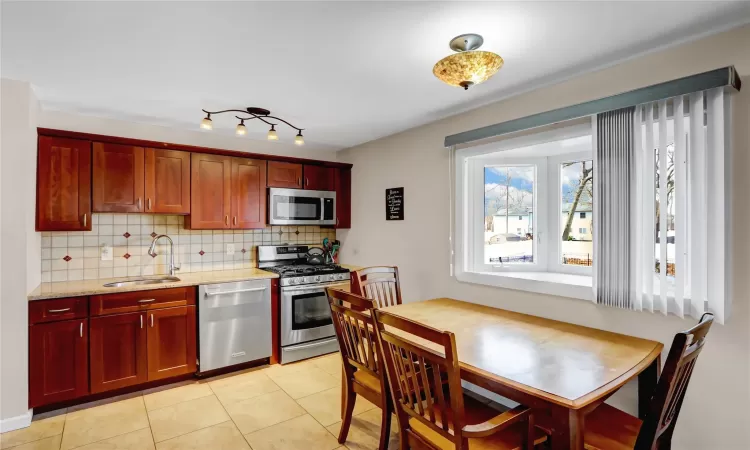 Kitchen with stainless steel appliances, reddish brown cabinets, a sink, and decorative backsplash