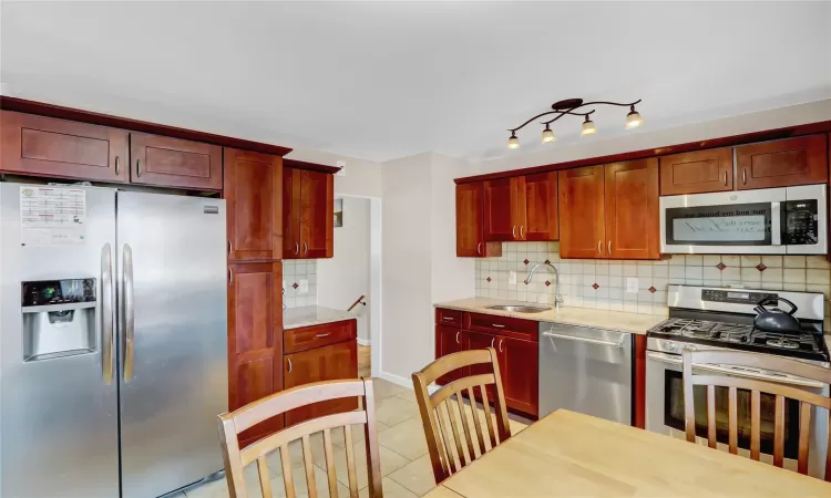 Kitchen with reddish brown cabinets, light tile patterned floors, tasteful backsplash, appliances with stainless steel finishes, and a sink