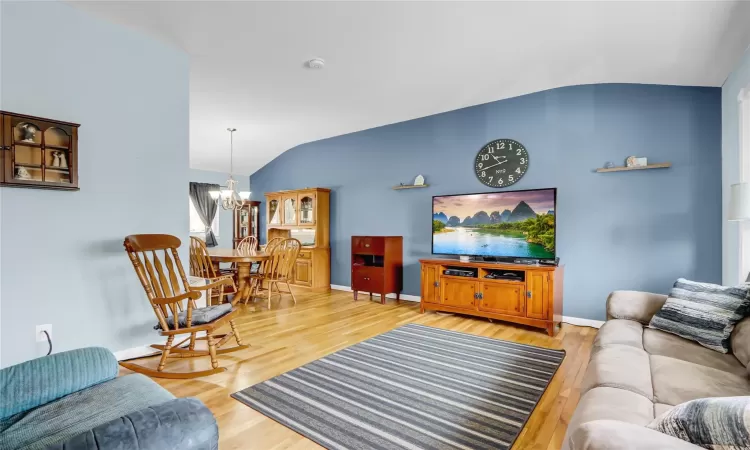 Living area featuring vaulted ceiling, a chandelier, light wood-style flooring, and baseboards