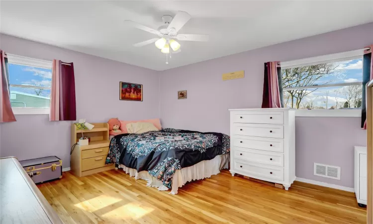 Bedroom featuring multiple windows, light wood-type flooring, visible vents, and baseboards