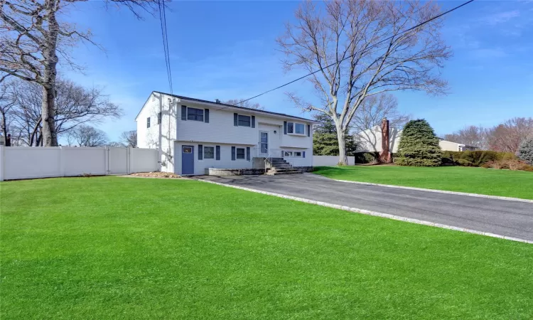 Back of house with aphalt driveway, fence, and a lawn