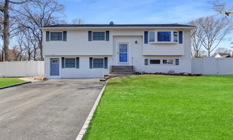 Bi-level home featuring aphalt driveway, a front lawn, fence, and a gate