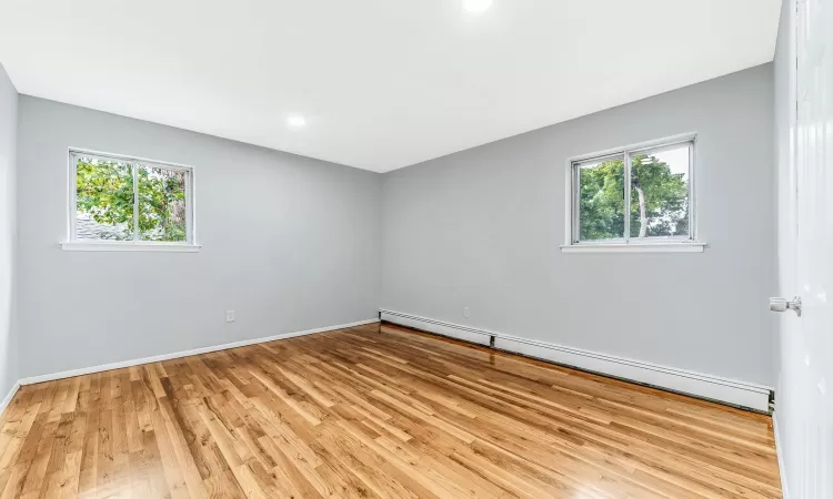 Spare room featuring a baseboard heating unit, plenty of natural light, wood finished floors, and baseboards