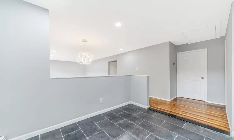 Spare room featuring attic access, baseboards, dark tile patterned floors, a notable chandelier, and recessed lighting