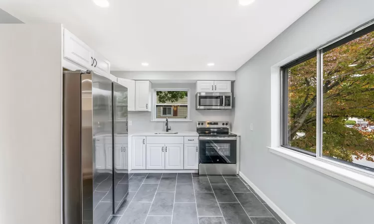 Kitchen featuring a sink, baseboards, white cabinets, light countertops, and appliances with stainless steel finishes