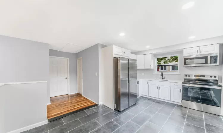 Kitchen featuring stainless steel appliances, light countertops, white cabinetry, a sink, and dark tile patterned floors