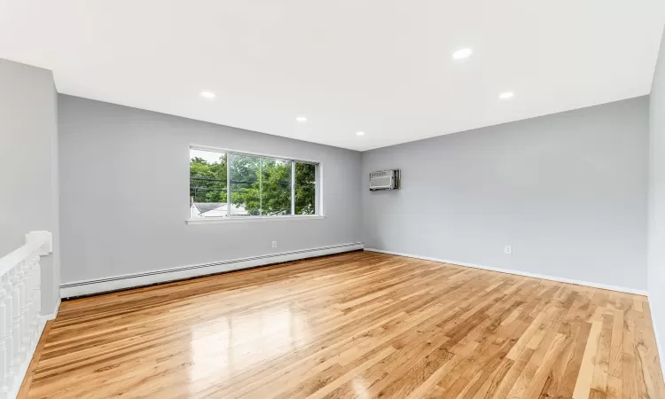 Unfurnished room featuring a baseboard radiator, baseboards, recessed lighting, and wood finished floors