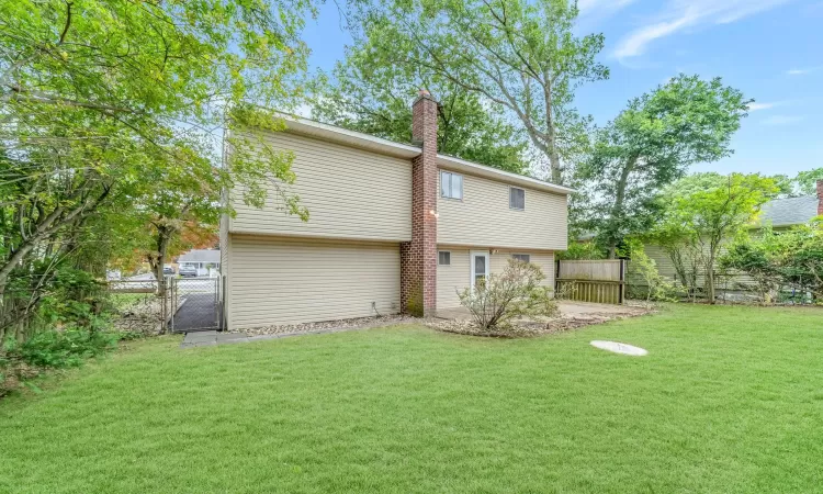 Back of property featuring a gate, a lawn, a chimney, and fence