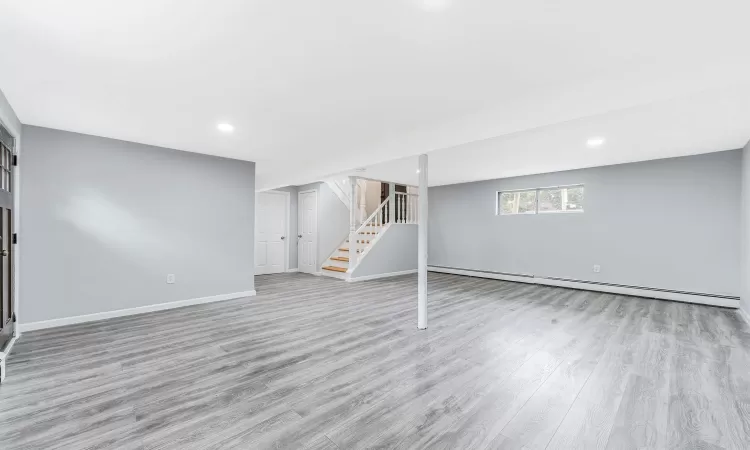 Basement with stairway, baseboards, a baseboard heating unit, and wood finished floors