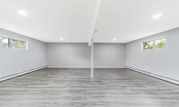 Below grade area featuring plenty of natural light, a baseboard heating unit, wood finished floors, and recessed lighting