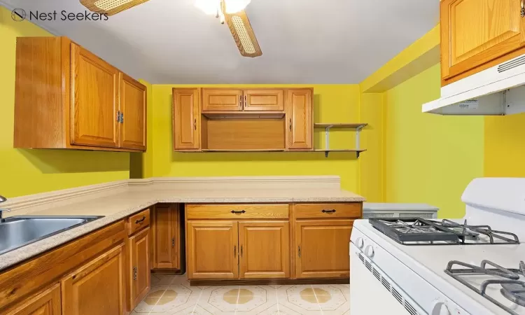 Kitchen featuring under cabinet range hood, a sink, light countertops, white range with gas stovetop, and ceiling fan