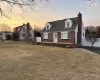 Cape cod home with brick siding, a front lawn, a chimney, and fence