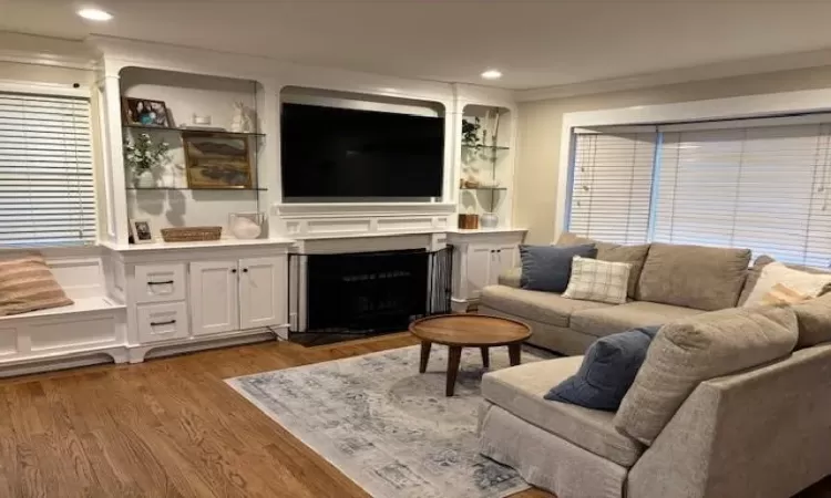 Living room featuring a fireplace with flush hearth, recessed lighting, dark wood-type flooring, and ornamental molding