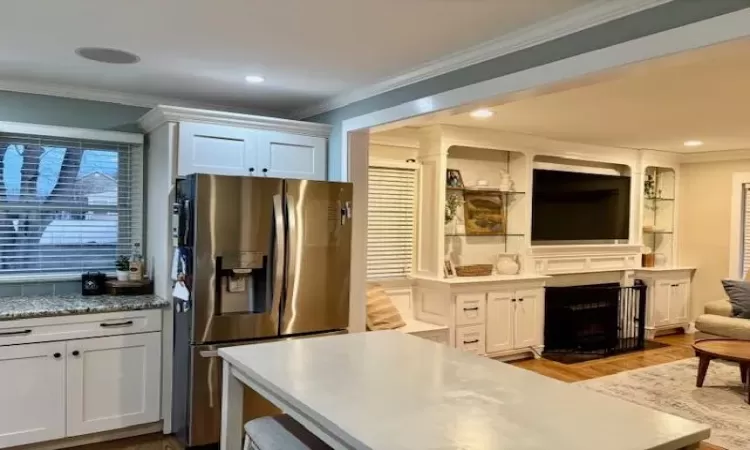 Kitchen with ornamental molding, a fireplace with flush hearth, stainless steel fridge with ice dispenser, and wood finished floors