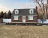 New england style home with brick siding, a front lawn, a chimney, and fence