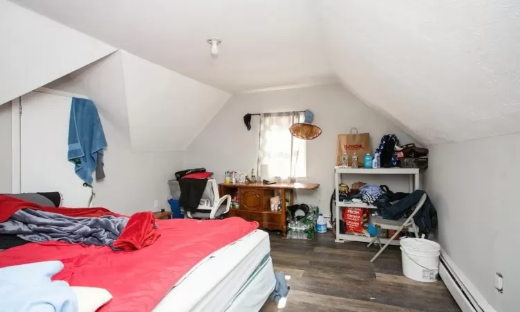 Bedroom with a baseboard heating unit, wood finished floors, and lofted ceiling