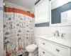 Full bath with toilet, a wainscoted wall, a shower with shower curtain, vanity, and tile walls