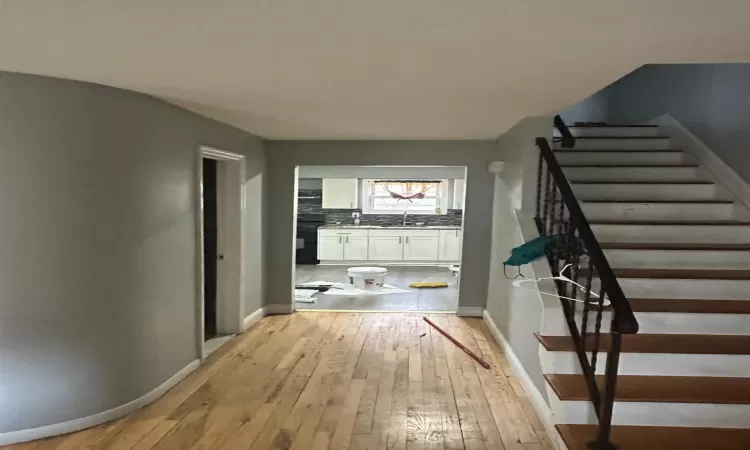 Hallway featuring light wood-style floors, a sink, baseboards, and stairs