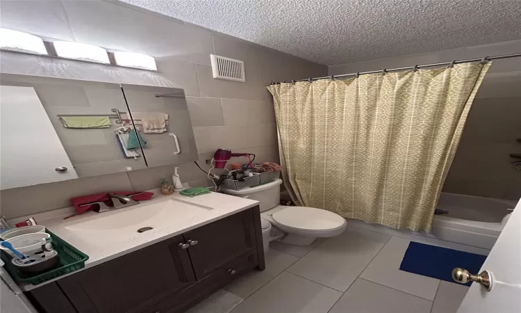 Full bathroom with tile walls, visible vents, toilet, a textured ceiling, and vanity