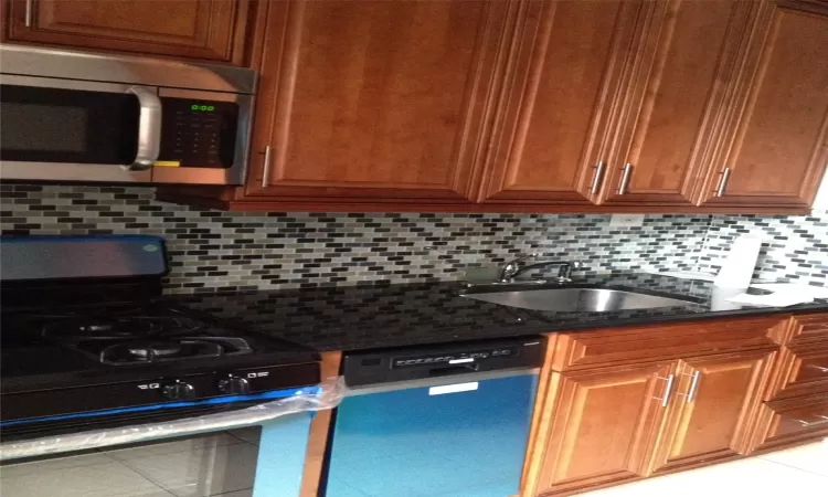 Kitchen featuring decorative backsplash, dark stone counters, appliances with stainless steel finishes, brown cabinets, and a sink