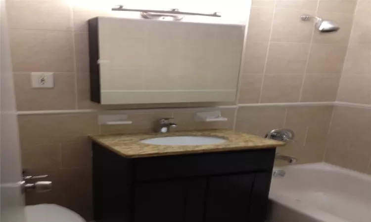 Full bath featuring tile walls, bathing tub / shower combination, tasteful backsplash, toilet, and vanity