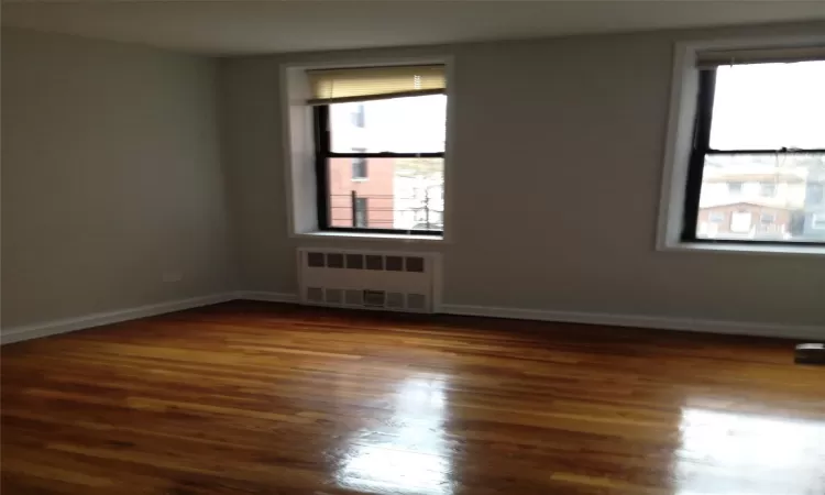 Unfurnished room featuring dark wood-style flooring, radiator heating unit, plenty of natural light, and baseboards