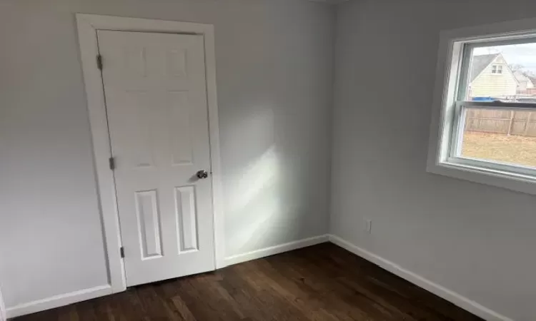 Unfurnished bedroom with multiple windows, baseboards, and dark wood finished floors