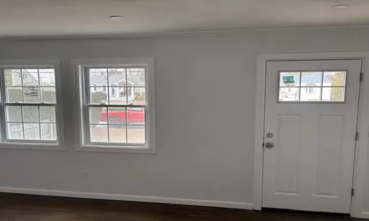 Entrance foyer with crown molding, dark wood-type flooring, and baseboards