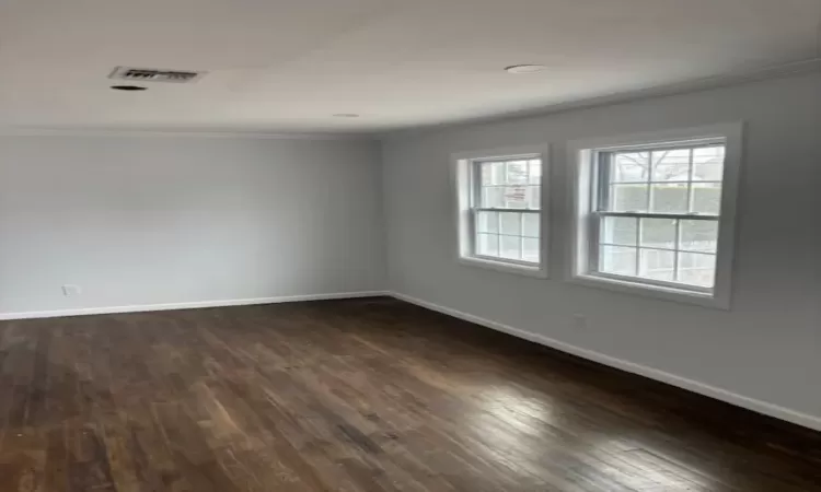 Empty room with baseboards, visible vents, dark wood finished floors, and crown molding