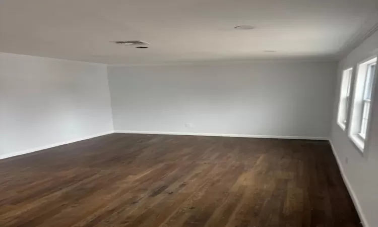 Empty room featuring ornamental molding, dark wood-type flooring, visible vents, and baseboards