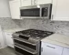 Kitchen with appliances with stainless steel finishes, light stone countertops, white cabinetry, and decorative backsplash