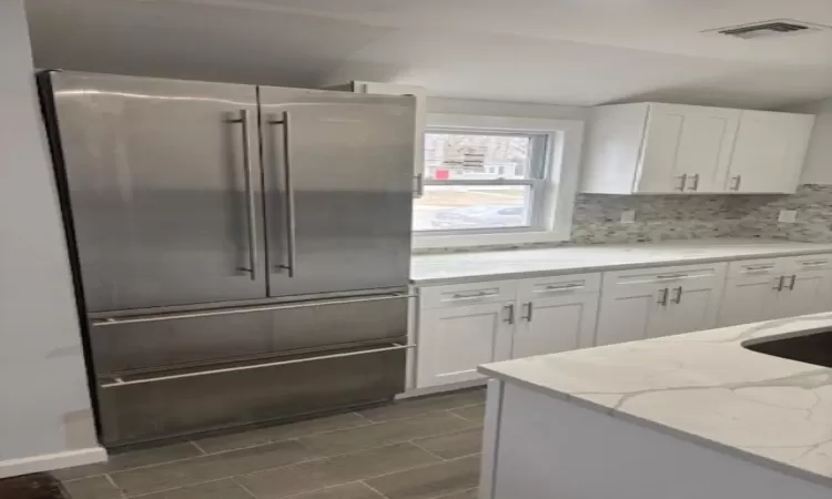 Kitchen featuring visible vents, light stone counters, high end fridge, white cabinetry, and backsplash