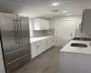 Kitchen with light stone counters, lofted ceiling, white cabinets, high quality fridge, and a sink